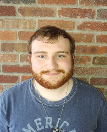 A man with a red beard standing in front of a brick wall.