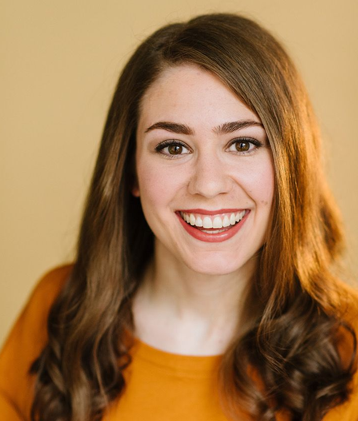A young woman smiling in an orange shirt.