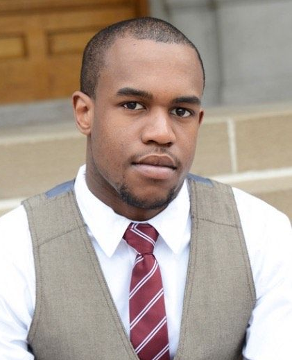 A black man in a vest and tie sitting on steps.